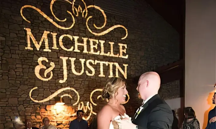 monogram2 A bride and groom share their first dance at their wedding; "Michelle & Justin" is illuminated on the stone wall behind them.