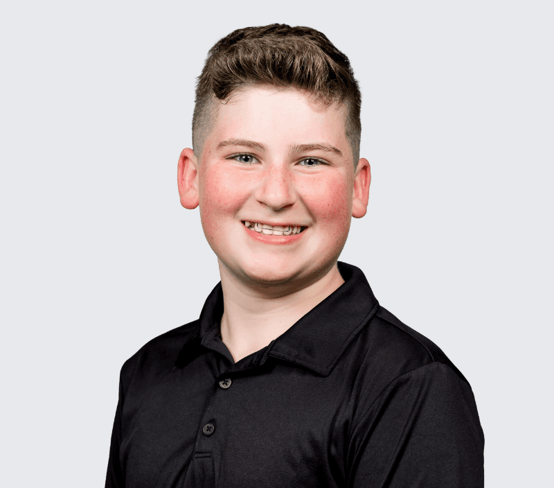 Smiling young person with short brown hair wearing a black collared shirt, posed against a plain light gray background.