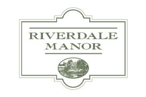A sign with the text "Riverdale Manor" in large capital letters, featuring an illustration of a manor house within an oval at the bottom.