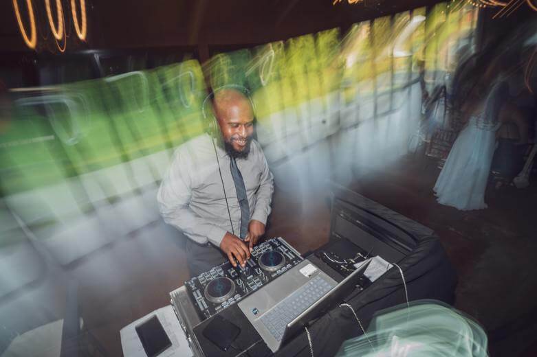 A DJ wearing headphones and a tie smiles while mixing music on a controller, with colorful light streaks surrounding him.