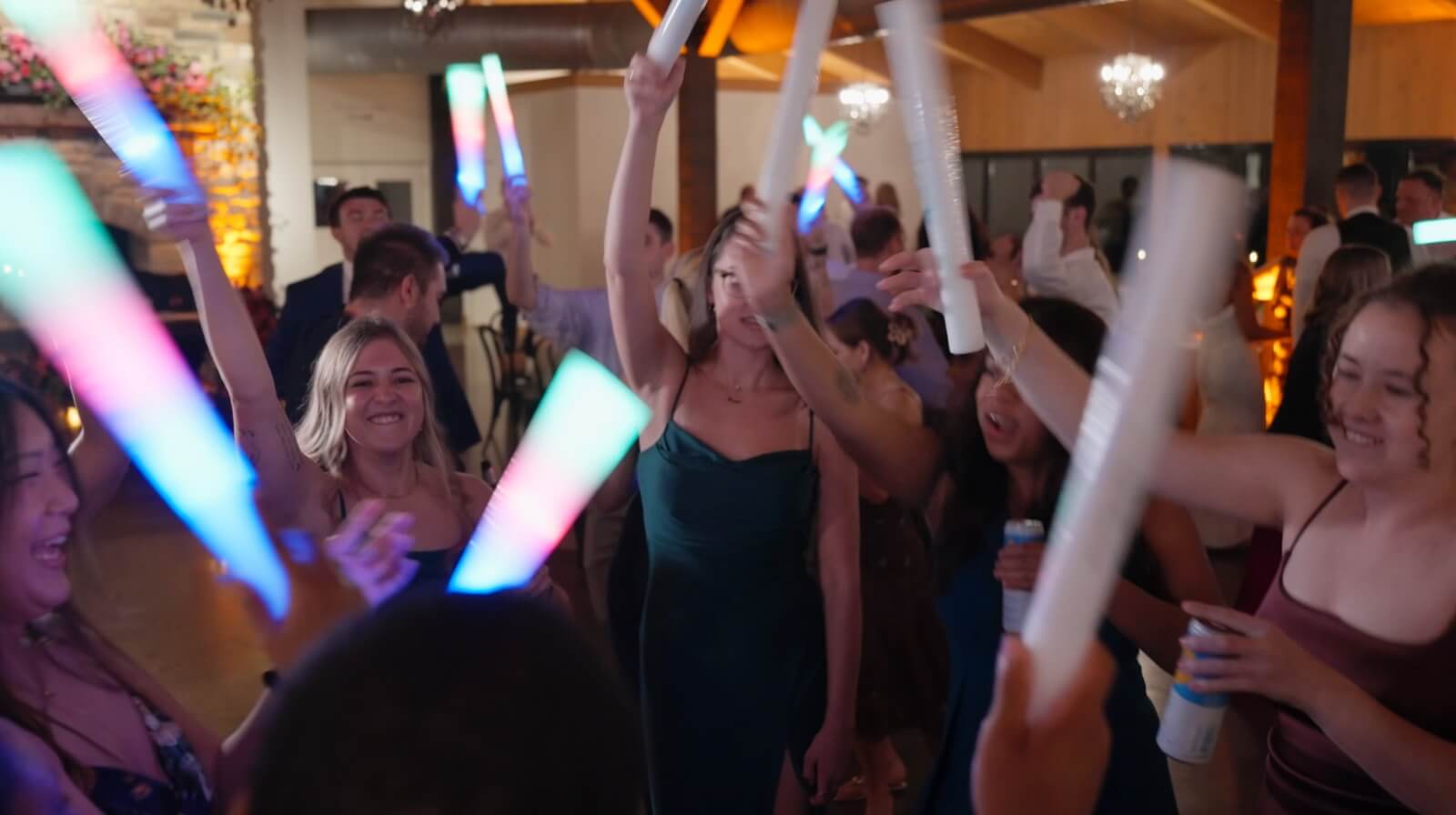 historic-acres-wedding-guests-dancing A group of people dance indoors at a party, holding up glowing, multicolored light sticks.
