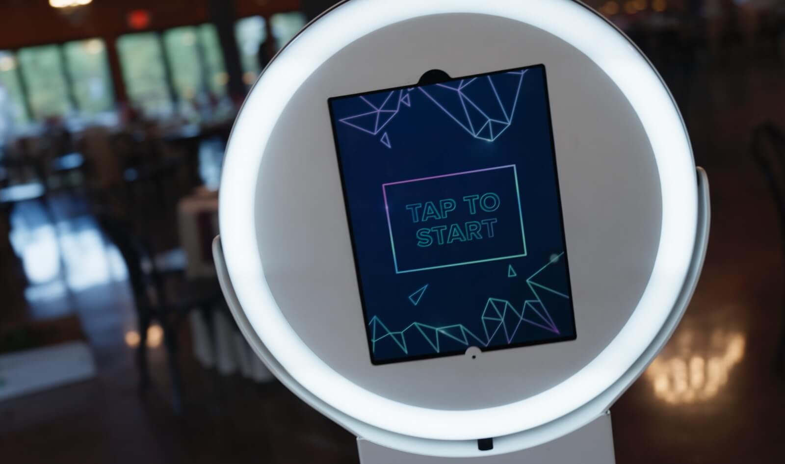 historic-acres-wedding-photo-booth A close-up of a digital photo booth with a circular LED light and a screen displaying "TAP TO START" in a geometric design.