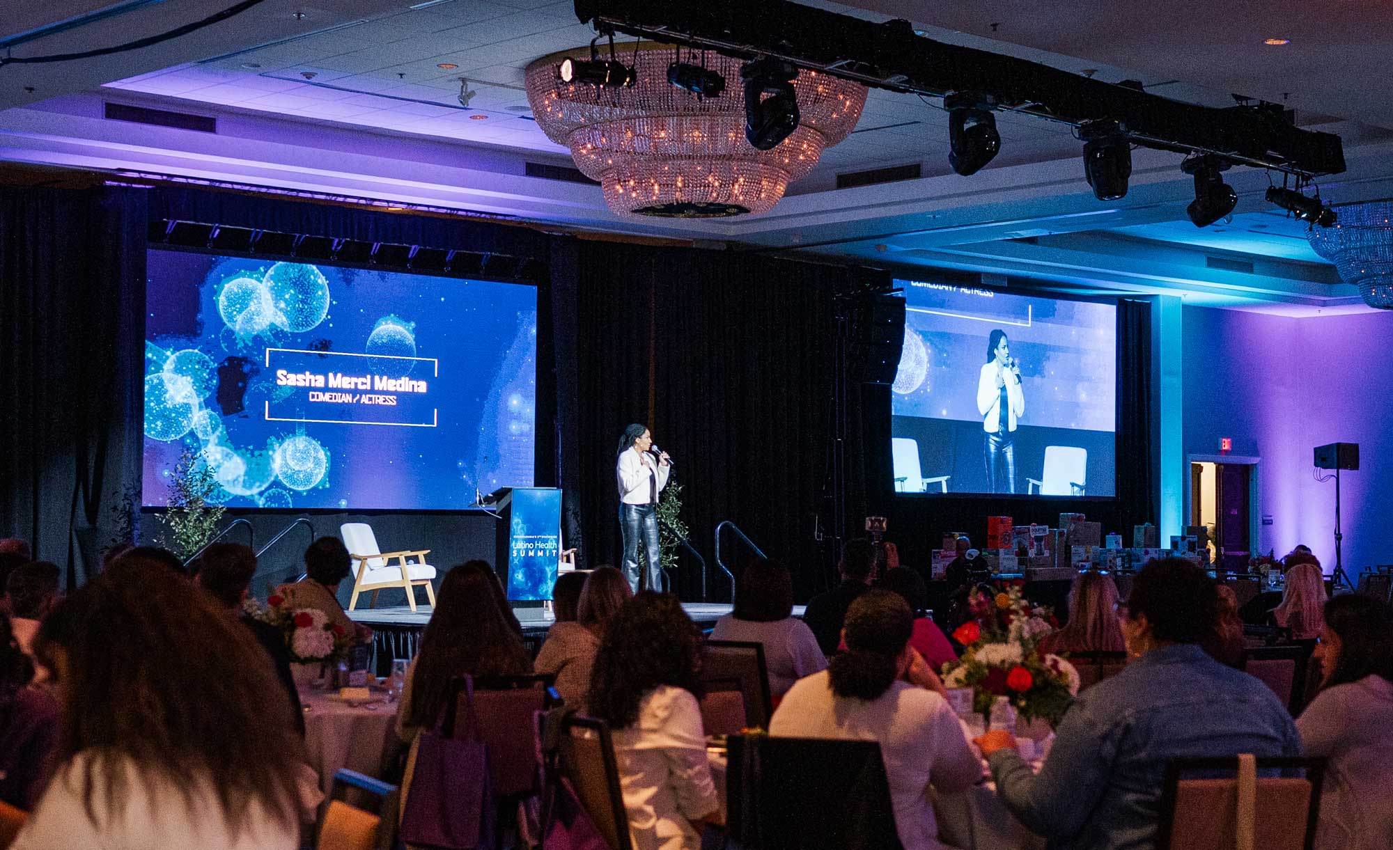 A speaker on stage before a seated audience at the Latino Health Summit