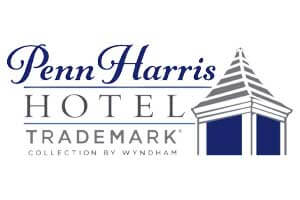 venue-logo-penn-harris Penn Harris Hotel Trademark Collection by Wyndham logo, featuring stylized text and a gray and blue illustration of a building roof.