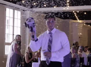 A man in a white shirt and tie holds a bubble machine at an indoor event while people sit at tables in the background at King Mansion in Harrisburg.