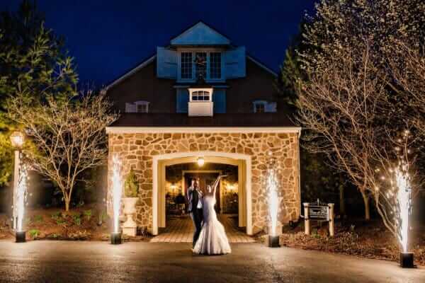 Bride and groom dancing outside a stone venue at night with fireworks on both sides of the entrance
