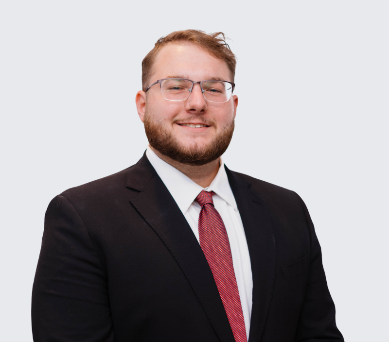 Andrew-26 A smiling man with a beard and glasses, wearing a suit and red tie.