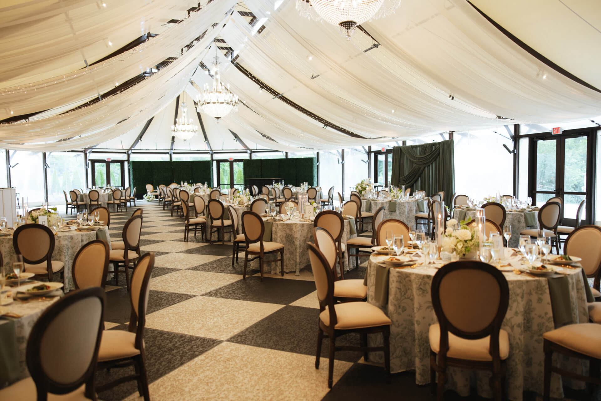 Beautiful indoor reception setup under a draped sailcloth tent with crystal chandeliers and a black and white checkerboard dance floor at The Willows at Ashcombe Mansion.