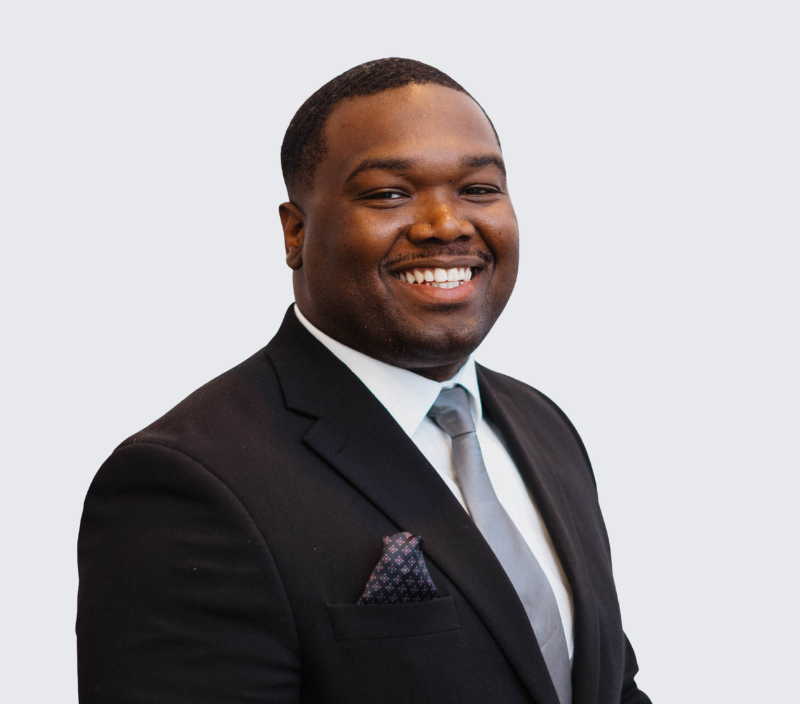 Phips-26 A smiling Black man in a black suit, white shirt, and grey tie.