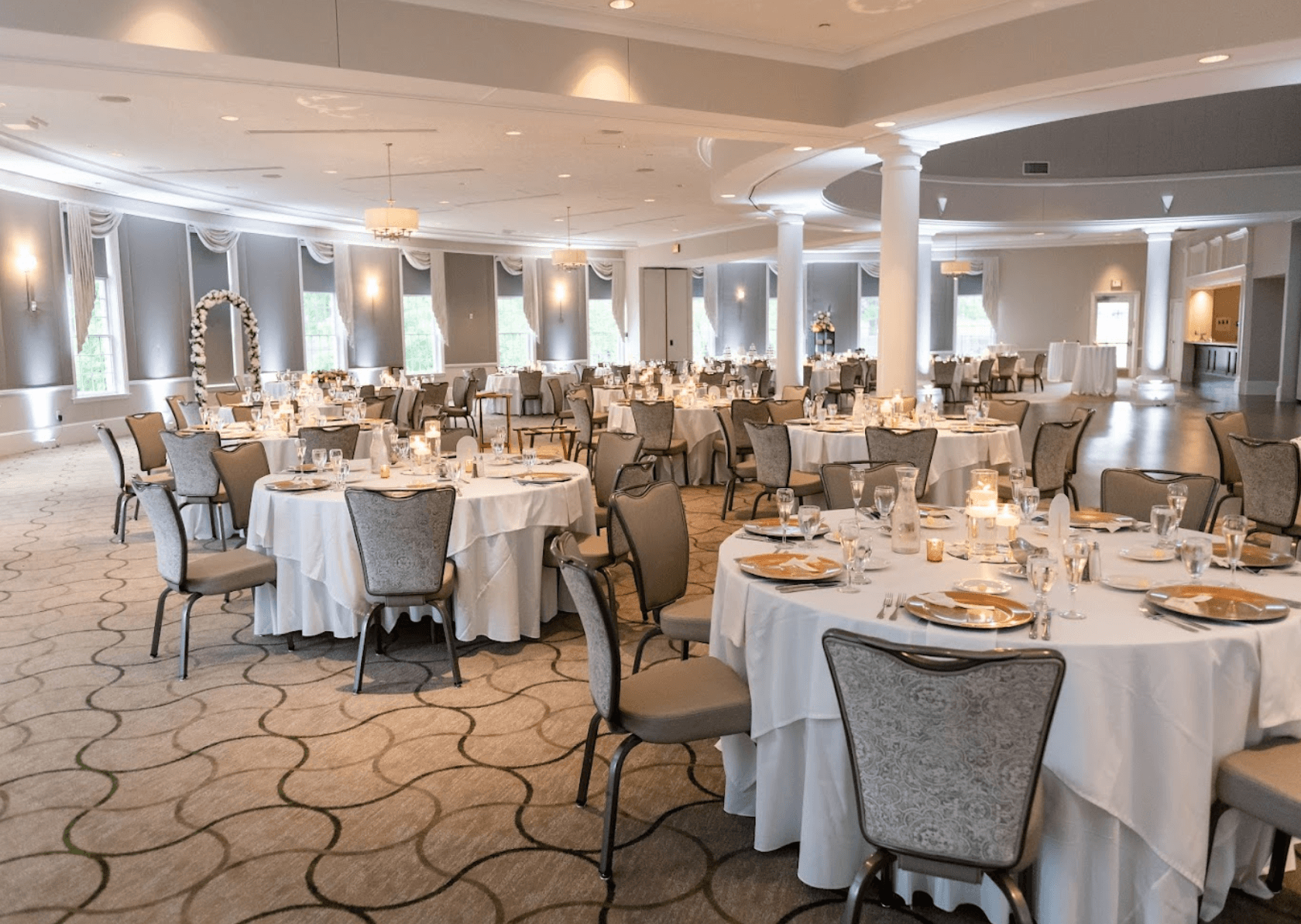 A large banquet hall set with multiple round tables covered in white tablecloths and prepared for a formal event at West Shore Country Club