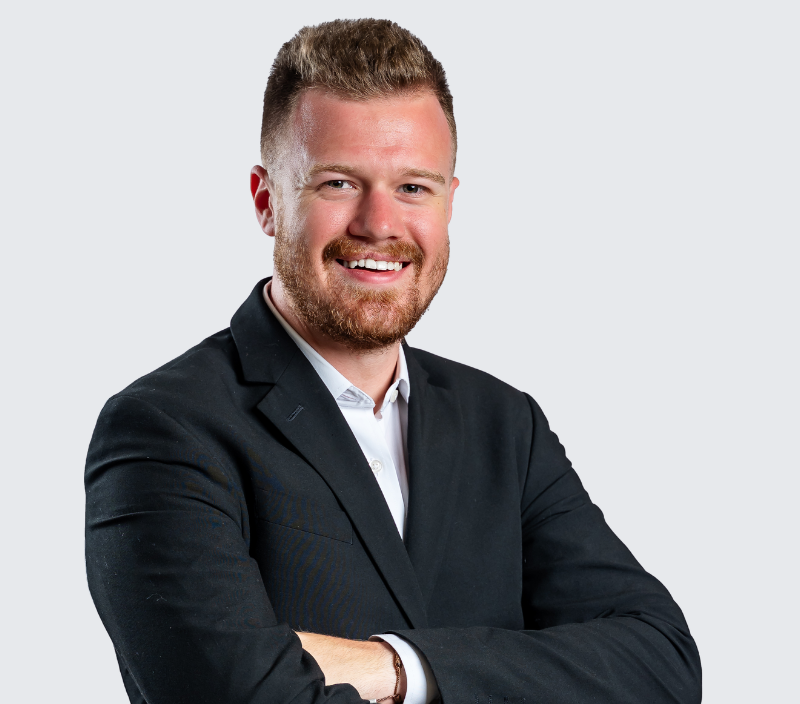 Tim_Nevil A smiling man with a beard wearing a black blazer and white dress shirt, arms crossed.