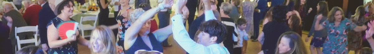 klock-hero-text-bkgd-128-still A group of people dancing at a party, with one person in the foreground holding a red hand fan.