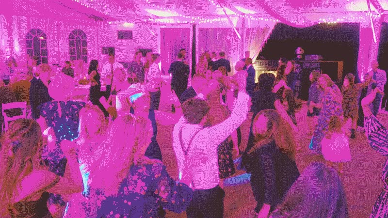 video-for-klock-mobile-1-still A large group of people dancing in a room lit with bright pink light.